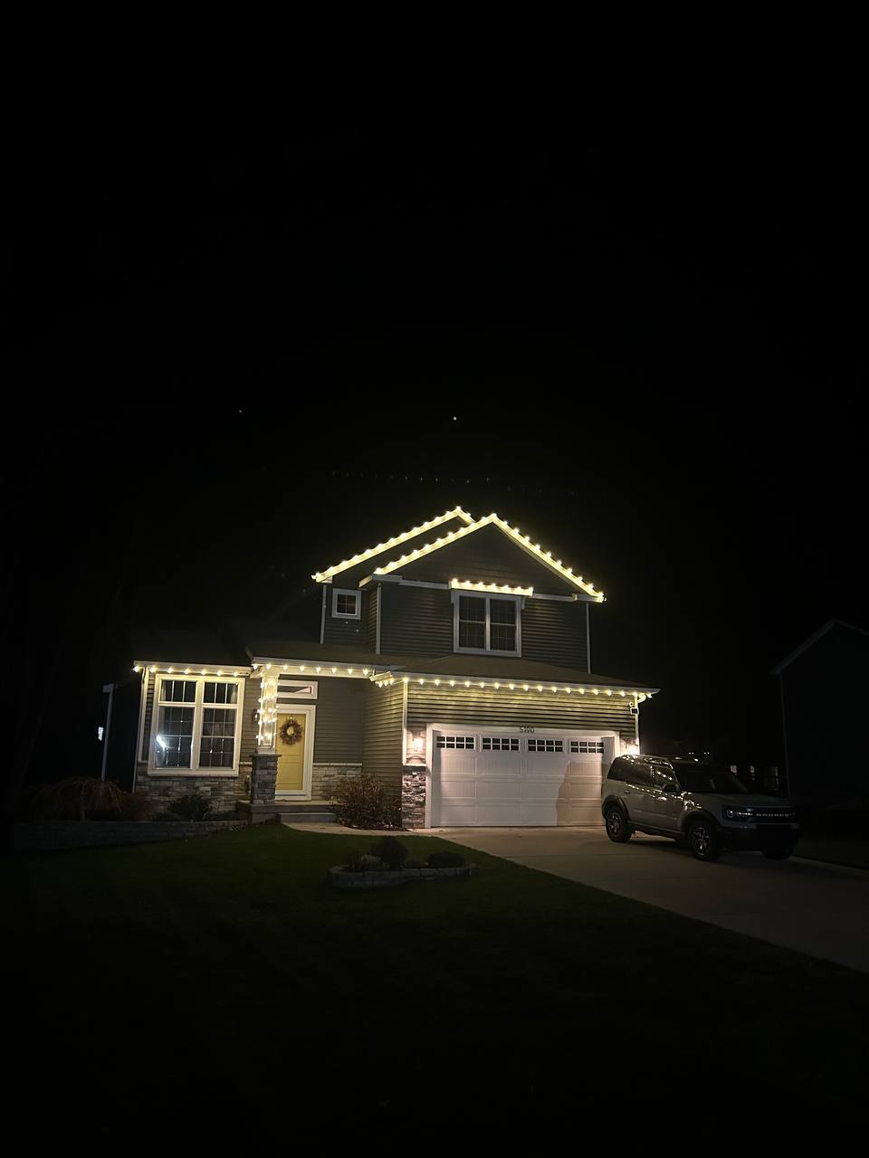 Warm white Christmas lights professionally installed along the roofline of an Ann Arbor-area home at night